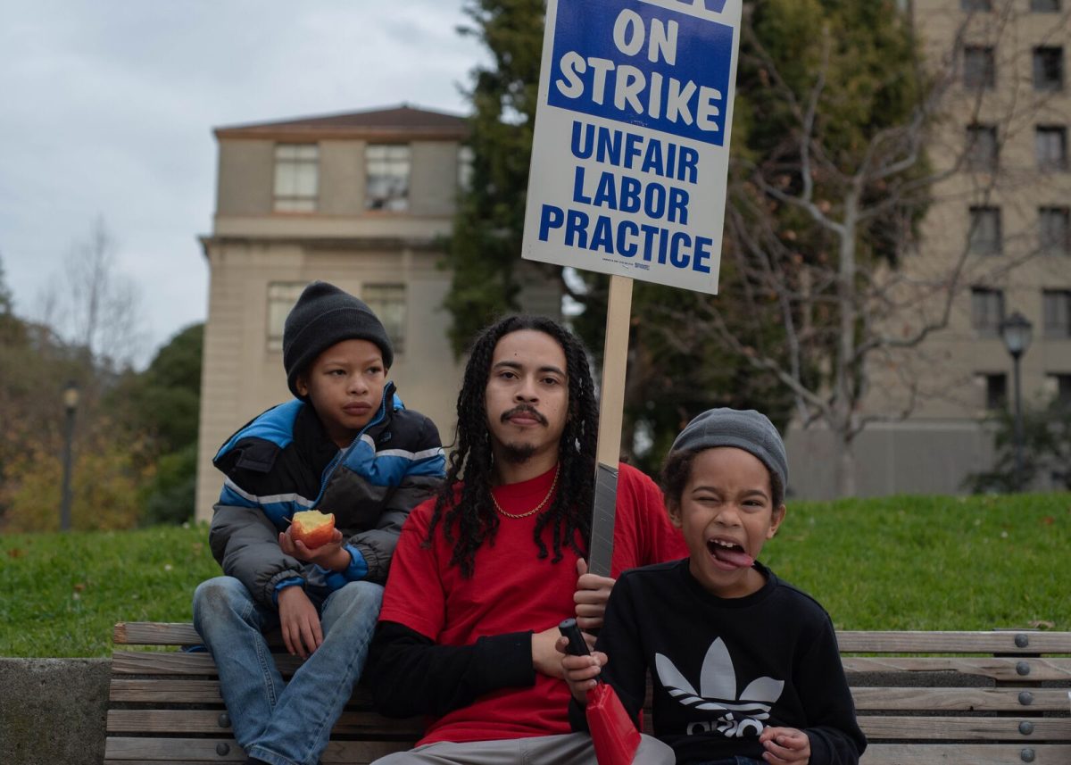 Vincente Perez, a striking fifth-year Cal doctoral student, photographed with his twin sons, Kaiyo (left) and Mikai (right), during a kid-friendly rally on Friday, Dec 9. Along with higher wages, the parents are asking for childcare subsidies and healthcare coverage for families.